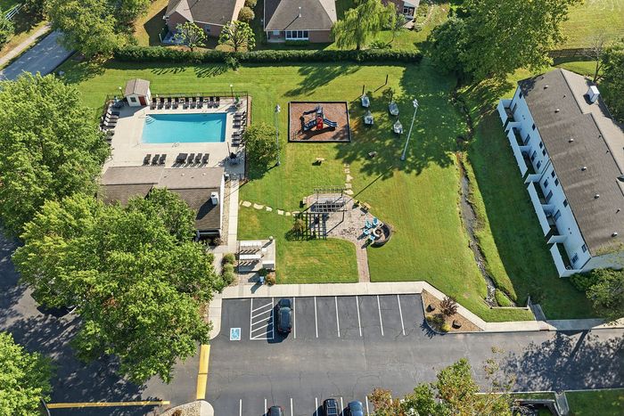 Picturesque aerial view of community amenities featuring a sparkling pool, modern playground, lush green spaces, and a convenient parking area.