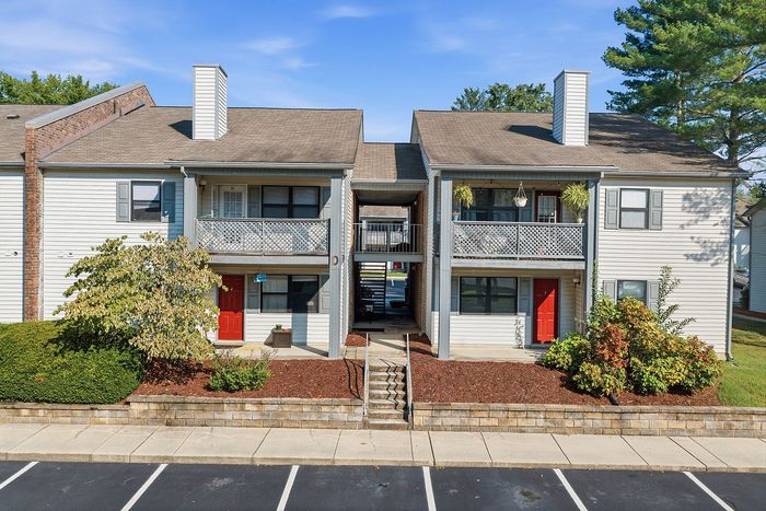 Charming two-story apartment building with vibrant red doors and decorative balconies, surrounded by lush landscaping and ample parking space.