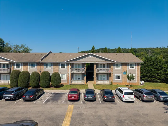 Charming apartment complex with manicured landscaping and ample parking, set against a lush green backdrop.