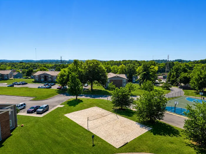 Scenic apartment complex with lush greenery, a sand volleyball court, and vibrant outdoor spaces.