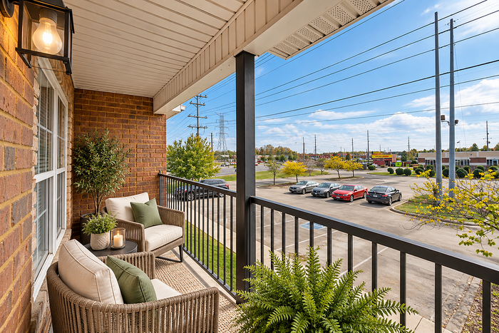 Inviting apartment balcony with cozy seating, lush greenery, and scenic view of a vibrant community.