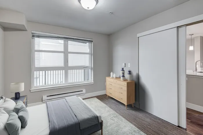 a spacious bedroom with a bed a dresser and a large window.