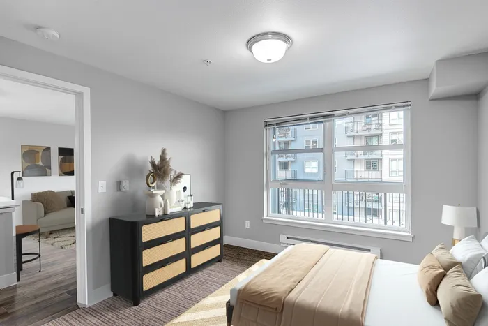 carpeted bedroom with queen bed and a dresser a large window and the view of the livingroom