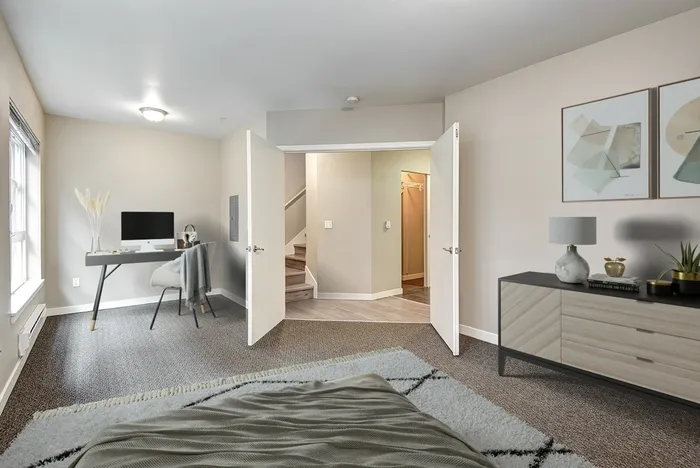 carpeted bedroom with a large dresser, a work desk with a monitor and a chair and two doors to enter
