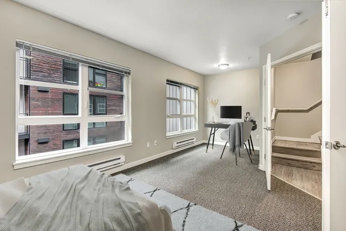 carpeted bedroom with queen bed and a desk with a computer, the room has large windows and two doors