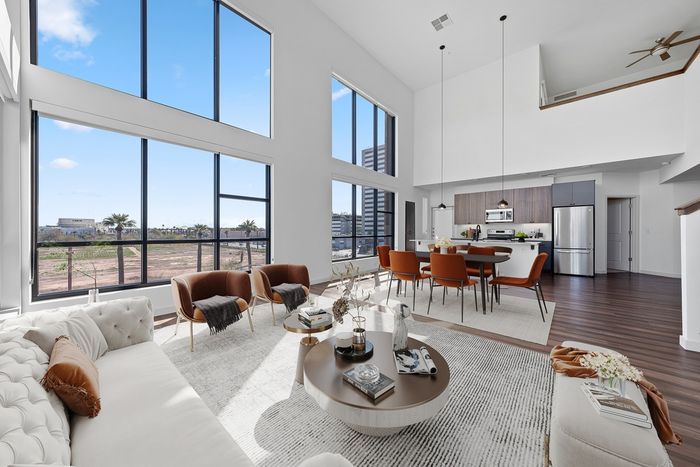 Callia living room facing kitchen, large winows, high ceiling, light fixtures, wood flooring, living room furniture with coffee table, dining table