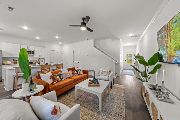 Furnished living rooms with rug, couch and lighted ceiling fan with view of kitchen with stainless steel appliacnes