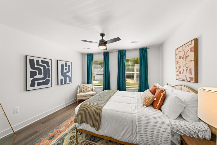 Furnished bedroom with bed, twowindows and lighted ceiling fan