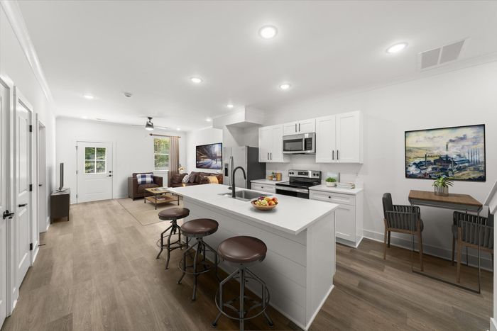 Furnished kitchen with kitchen island and barstools, stainless steel and black appliances, white cabinets, and a view of the living room