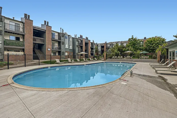 Inviting outdoor pool surrounded by modern apartment buildings and lounge chairs under a clear blue sky.