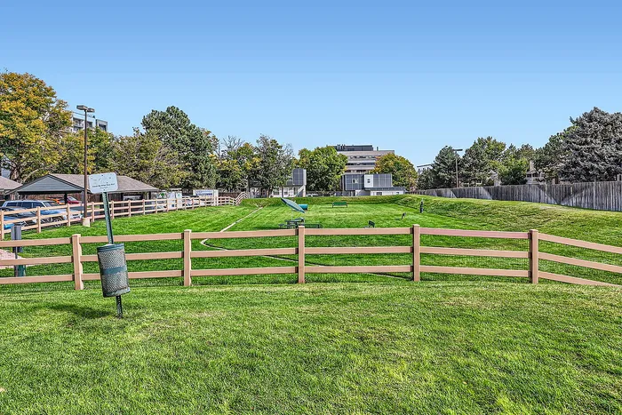 Vibrant green community park surrounded by trees and modern apartments, featuring ample open space and benches.