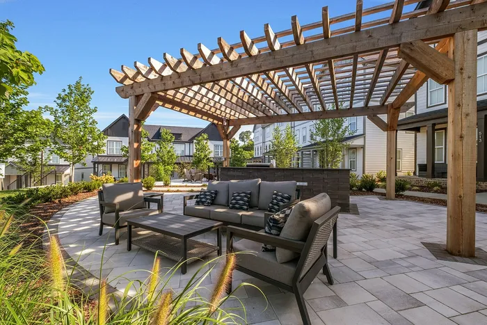 Charming outdoor patio with elegant wooden pergola and comfortable seating, surrounded by lush landscaping and modern townhouses.