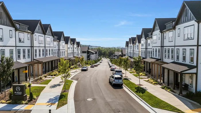 Charming suburban street lined with elegant townhomes, lush greenery, and clear blue skies.