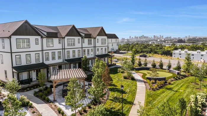 Charming townhomes with a lush garden view, featuring a pergola and scenic city skyline in the distance.