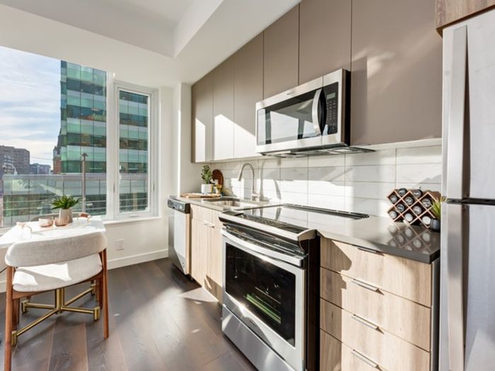 A bright One Park Central apartment kitchen with stainless steel appliances, light wood cabinets, and large windows allowing natural light to fill the space.