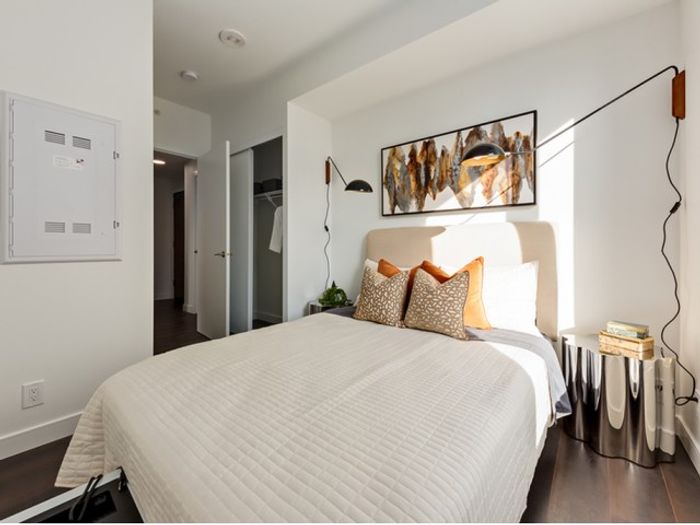 A cozy One Park bedroom with a plush bed, soft neutral tones, warm lighting, and decorative wall art, creating a relaxing ambiance.