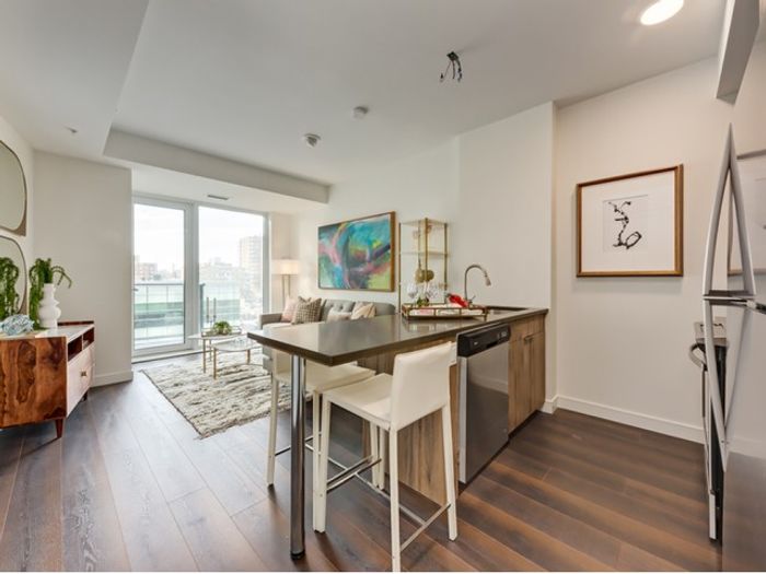 An open-concept living and dining space at One Park featuring a kitchen island with barstools, a cozy seating area, and floor-to-ceiling windows letting in natural light.