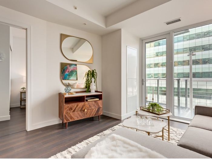 A bright living room at One Park with glass doors leading to a private balcony, modern wood furniture, and contemporary artwork on the wall.
