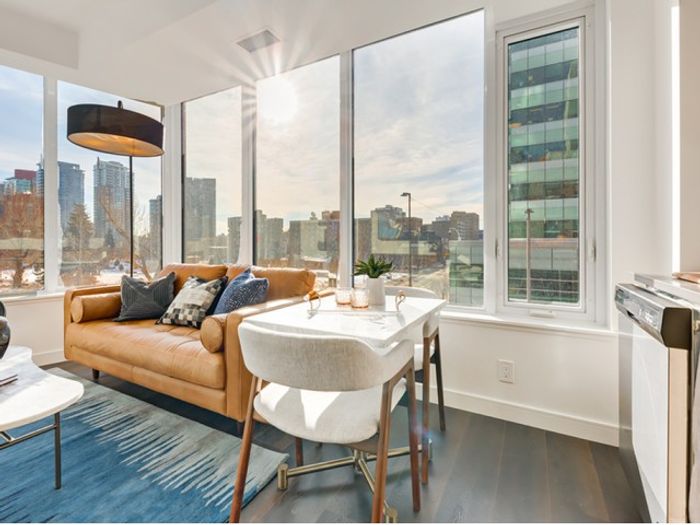 Bright and modern apartment living room at One Park Central with floor-to-ceiling windows, city views, a tan leather couch, dining table, and contemporary lighting.