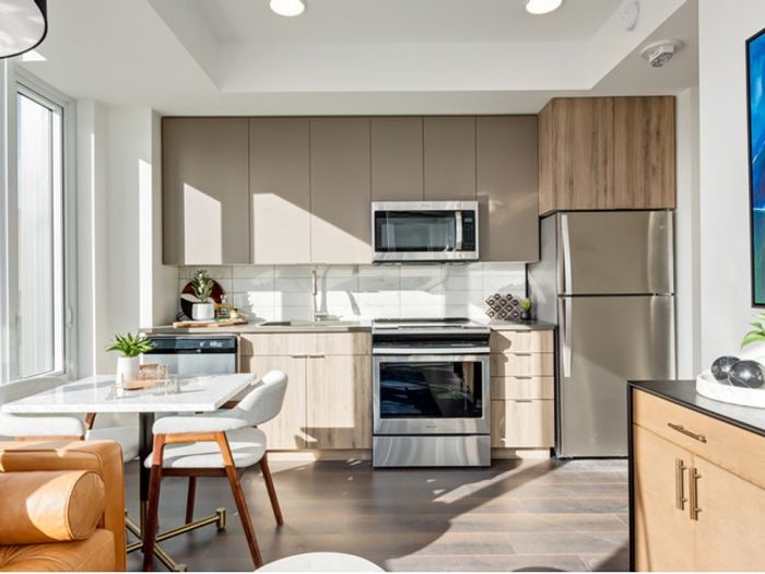 Modern kitchen and cozy dining nook at One Park featuring light wood cabinetry, stainless steel appliances, and large windows with city views.