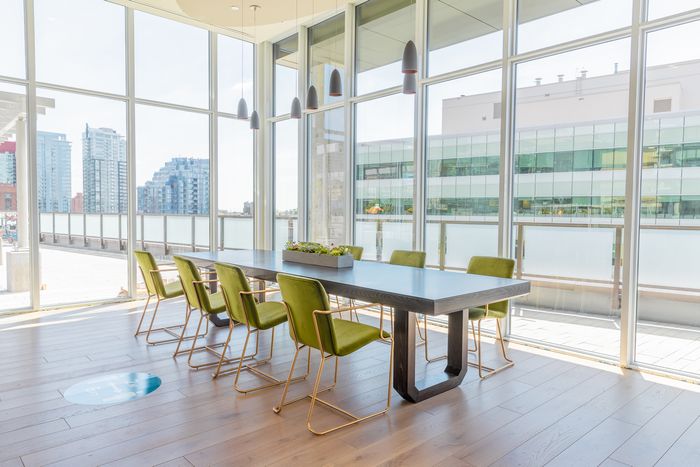 Bright conference room with a large table surrounded by green chairs and floor-to-ceiling windows overlooking a cityscape.