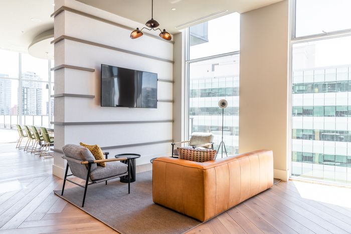 A bright lounge area with a mounted flat-screen TV, modern wood-accented furniture, and large floor-to-ceiling windows allowing in natural light.