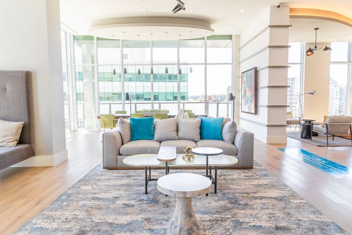 A vibrant resident lounge with colorful accent pillows, a white coffee table, a modern chandelier, and floor-to-ceiling windows offering ample natural light.