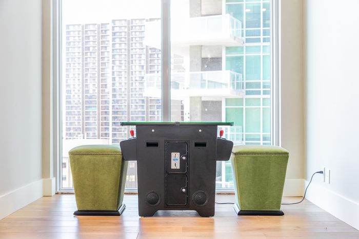 Game table positioned between two green stools in a bright, modern room with floor-to-ceiling windows overlooking a cityscape.