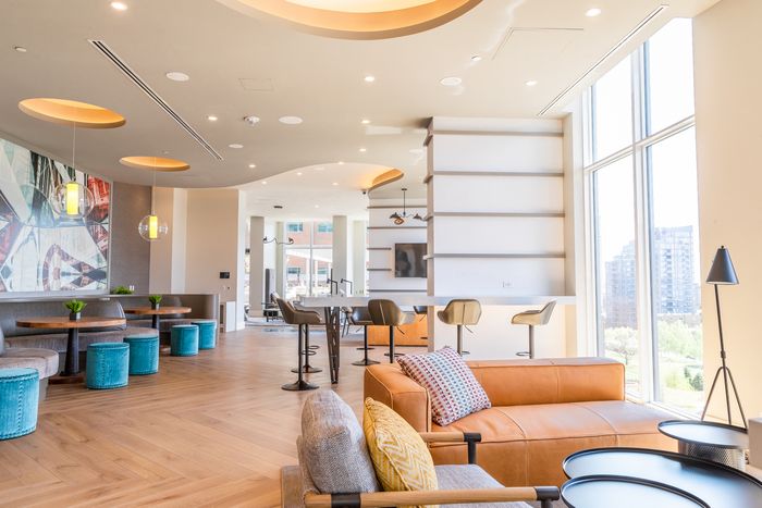 Sunlit resident lounge with cozy seating, high-top tables, and modern decor, featuring soft neutral tones and floor-to-ceiling windows.