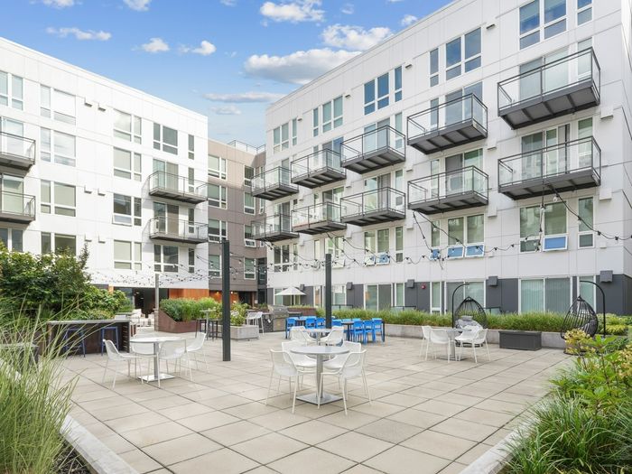 Spacious apartment courtyard with outdoor tables, string lights, grills, and surrounding garden beds