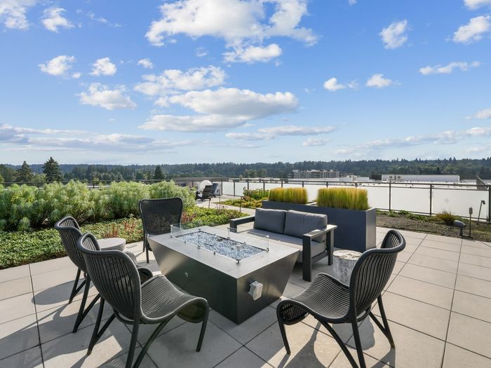 Rooftop patio with modern black chairs, a fire pit table, cushioned seating, and panoramic views of trees and buildings