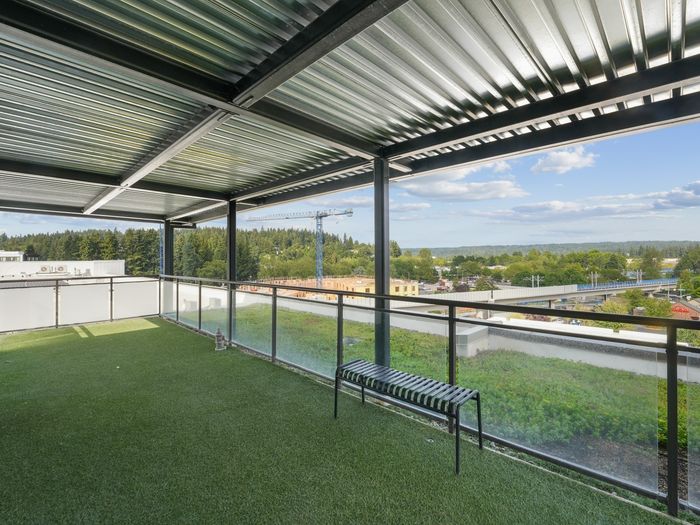 Rooftop pet run with artificial turf, metal bench, and partial cover, overlooking trees and cityscape.
