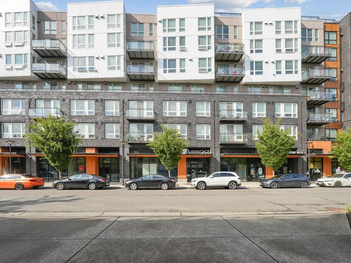 Modern multi-story apartment building with balconies, large windows, and retail shops at street level.
