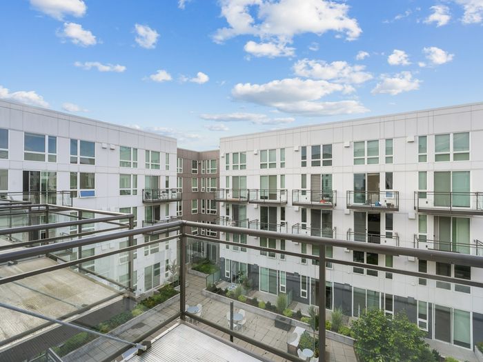 Modern apartment complex with glass balconies overlooking a landscaped central courtyard and seating areas