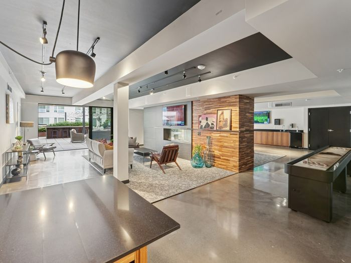 Modern resident lounge featuring lounge seating, flat-screen TVs, shuffleboard table, and direct courtyard access.