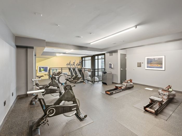 Gym space with stationary spin bikes, rowing machines, and elliptical trainers, located on an upper-level balcony area