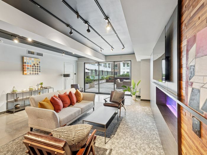 Bright resident lounge featuring a beige sofa with colorful throw pillows, accent chairs, modern decor, a flat-screen TV, and large glass doors opening to an outdoor courtyard