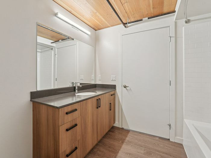 Clean, modern bathroom featuring a wood vanity with black hardware, large mirror, integrated sink, white tile shower, and natural wood ceiling