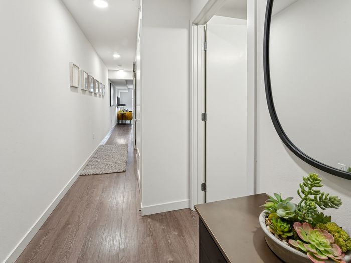 Bright hallway with wood flooring, a decorative rug, framed artwork on the wall, a round mirror, and a console table with a potted succulent arrangement