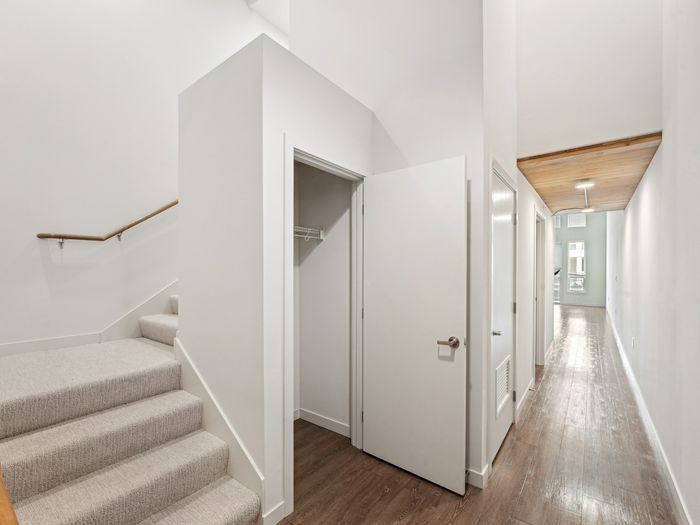 Entryway featuring wood flooring, a staircase with carpeted steps and wooden railing, open closet with shelving, and hallway leading to bright windows with natural light