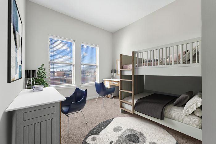 Children&rsquo;s bedroom featuring bunk beds, two desks with lamps, two navy chairs, a bear-themed rug, and large windows letting in natural light.