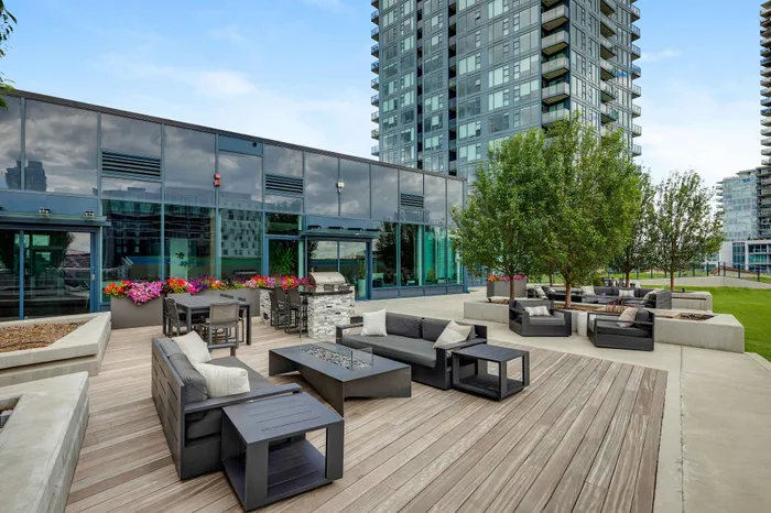 Modern outdoor lounge area with sleek seating, vibrant flowers, and a stylish grill setup, perfect for entertaining against a backdrop of luxury high-rise apartments.
