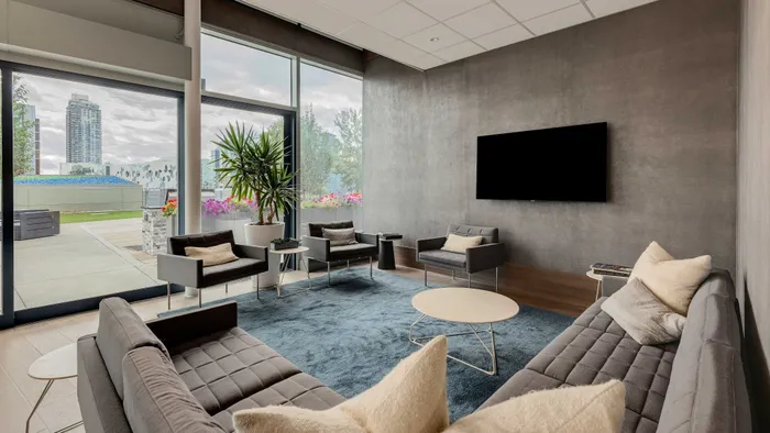 Elegant and modern living room with large windows offering cityscape views, featuring stylish gray seating, decorative plants, and a plush area rug.