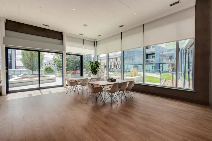 Modern dining area with large windows offering a bright and airy ambiance, featuring sleek wooden flooring and chic seating with views of a landscaped terrace.