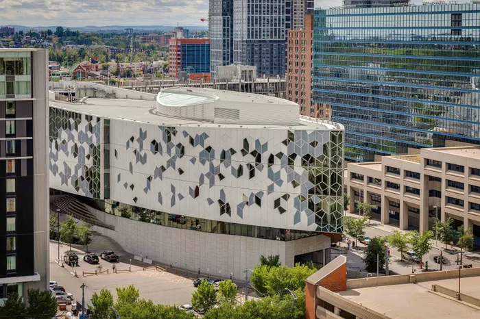 Modern architectural marvel with geometric facade design, located in a vibrant urban setting with lush greenery and skyline views.