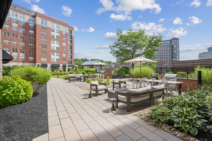 Charming urban apartment complex with a beautifully landscaped patio, cozy seating areas, and vibrant greenery under a clear blue sky.