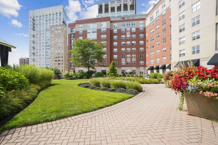 Beautiful urban garden pathway surrounded by lush greenery and vibrant flowers in a modern apartment complex courtyard.