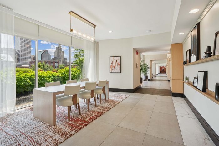 Elegant dining area with modern furnishings and panoramic city views through large glass windows, creating a bright and inviting atmosphere.
