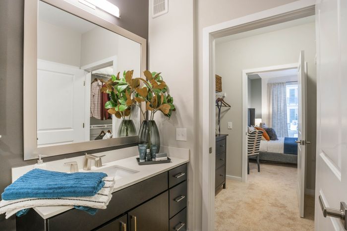 Contemporary bathroom with elegant vanity mirror and lush greenery leads to a cozy bedroom with natural light and modern decor.