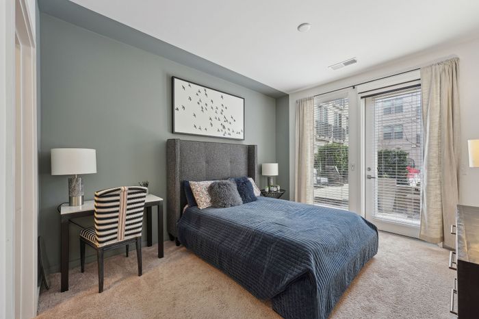 Bright and elegant bedroom featuring a cozy queen bed, stylish wall art, and ample natural light from glass doors with garden view.